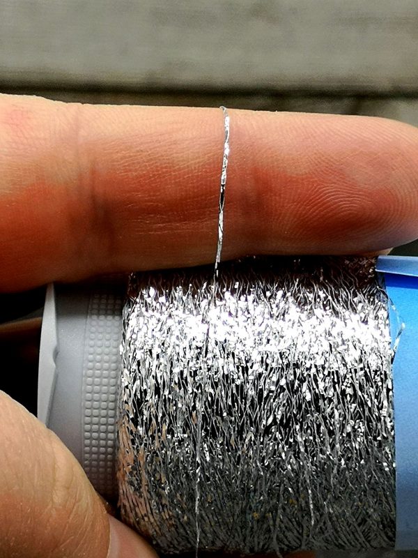 Metallisiertes Polyestergarn auf Kone in silber über den Finger gelegt